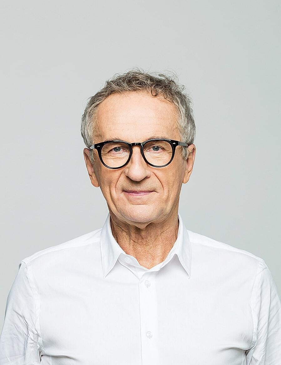 Smiling older man in glasses, white shirt.